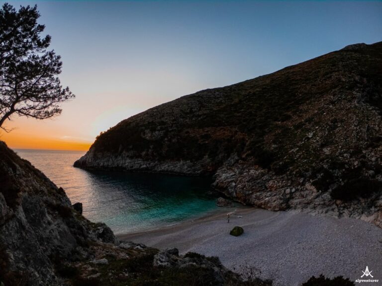 Dafina Bay’s sheltered turquoise cove and pebbled beach at sunset, framed by rocky hills