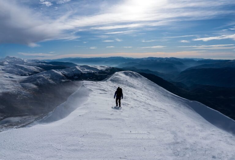 A hiker crosses the snowy ridge of Gjallica mountain above the surrounding Northern Albanian ranges