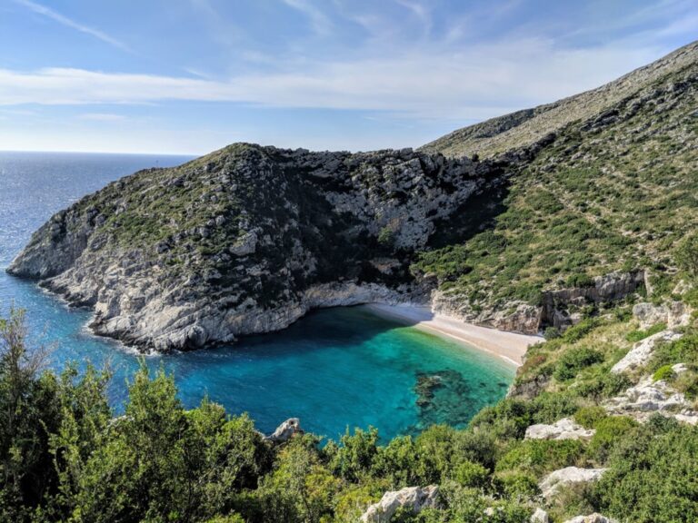 Turquoise water and a small beach beneath rocky hills at Grama Bay on Albania’s Karaburun Peninsula