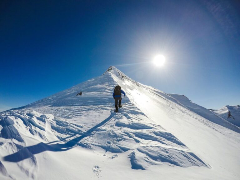 A hiker climbs the snowy ridge of Gramos in bright winter sunlight