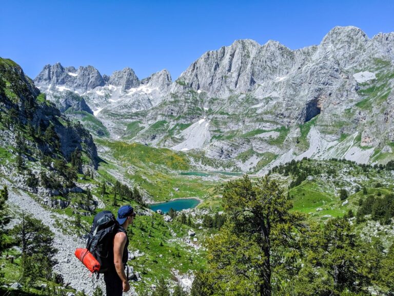 A hiker above a turquoise lake beneath the rocky peaks of the Jezerca Lakes in Albania