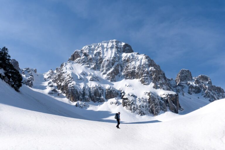 A hiker crosses a snowy slope below the rugged peaks of Maja e Boshit in winter