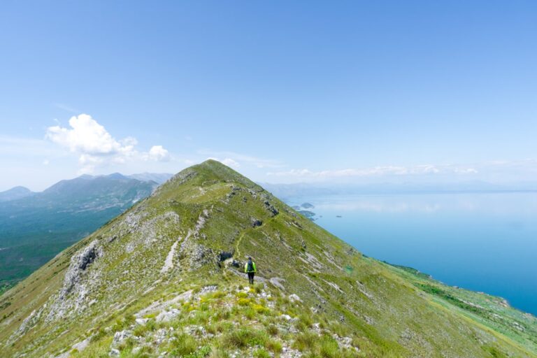 A hiker follows the rocky green ridge of Maja e Taraboshit above the blue Adriatic Sea
