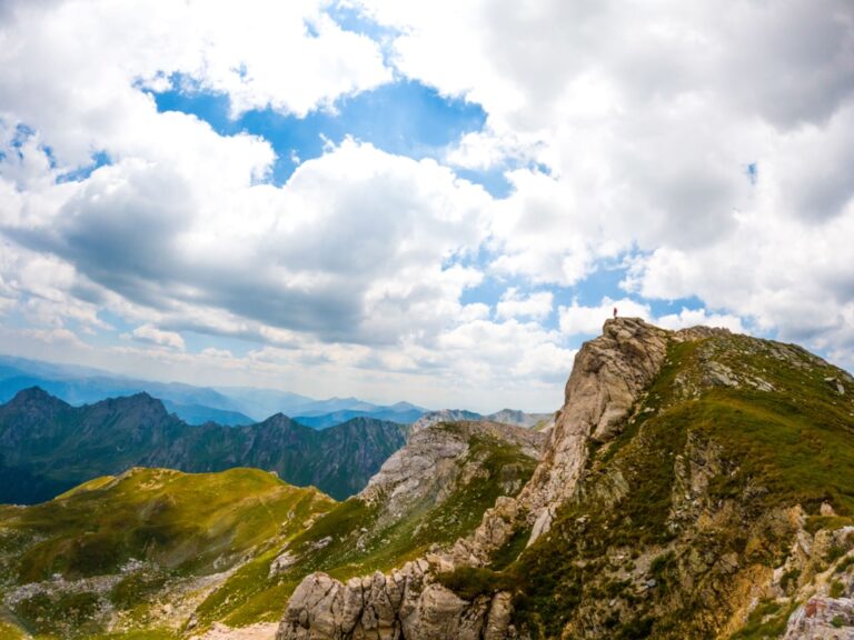 Rocky green ridges on Mount Korab beneath a cloudy blue sky, with distant mountain ranges