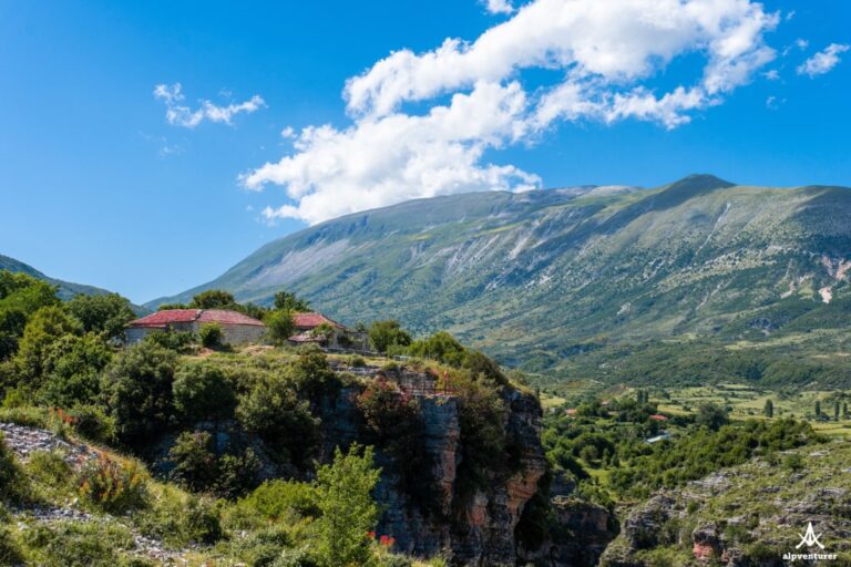 Guesthouse above Nivica Canyon, with a rocky gorge and green mountains beneath a blue sky