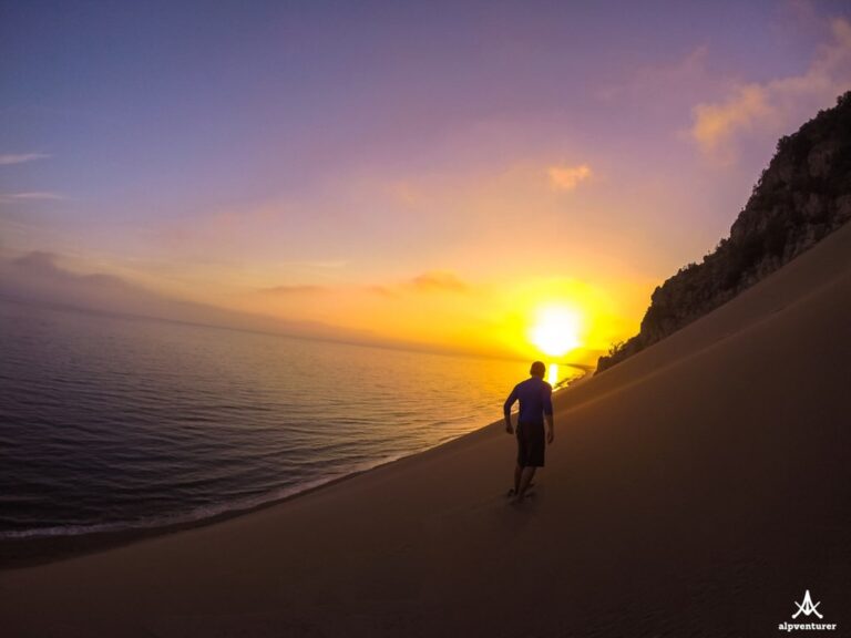 A hiker walks along the shore at Rana Hedhun as the sun sets over the sea