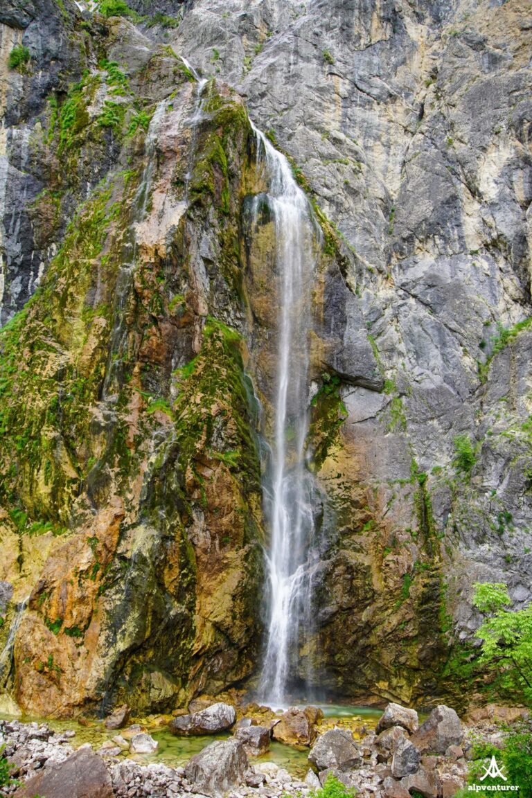 Selca Waterfall streams down a steep gray rock face into a shallow pool among boulders