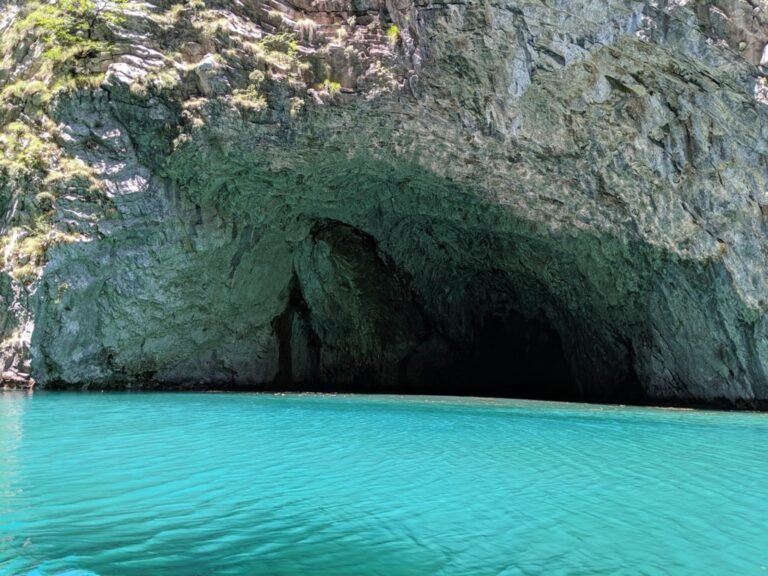 Turquoise water at the Shala River beneath a large shadowed cave in a rocky cliff