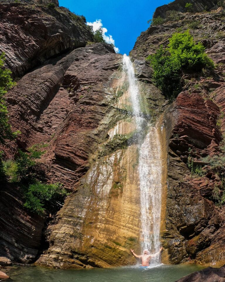 Shëngjergj Waterfall pours down a rocky cliff into a pool beneath a clear blue sky