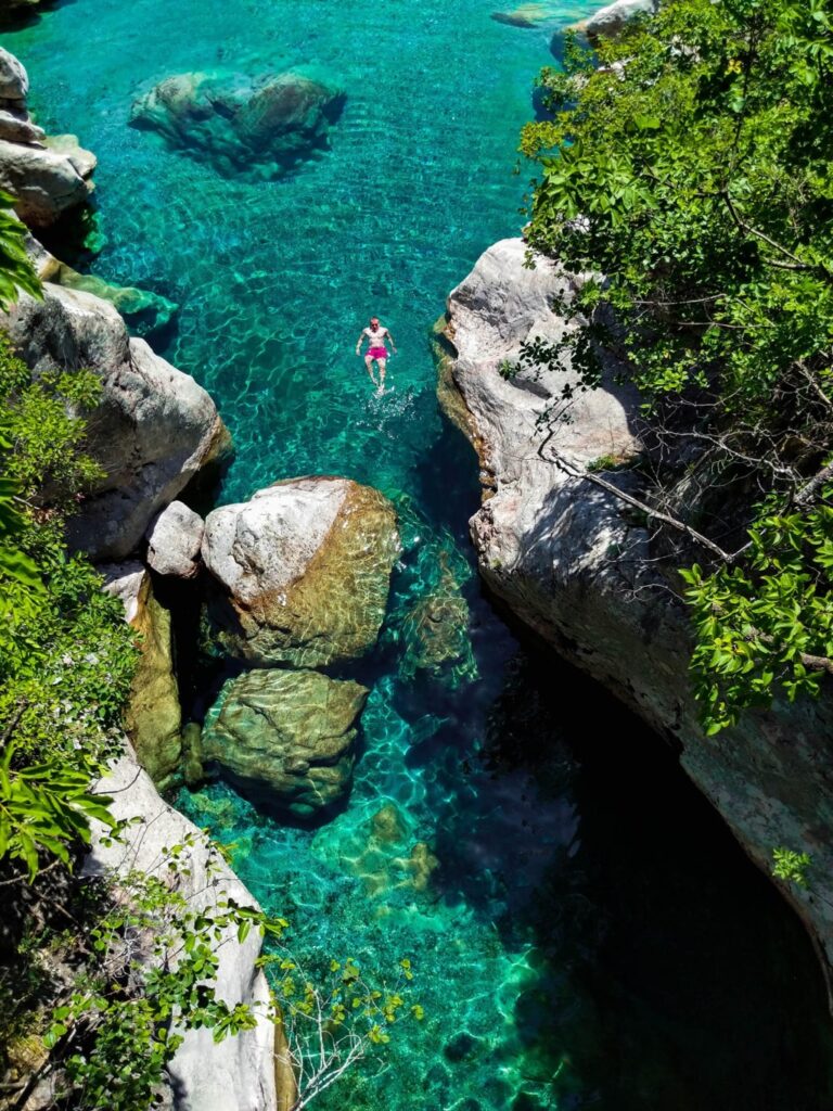 A hiker swims in clear turquoise pools between pale rocks at Nderlysa in Theth