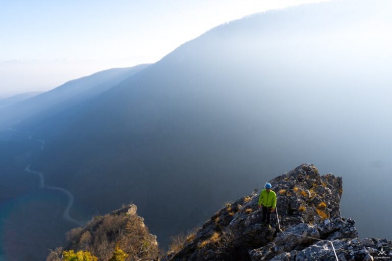 A hiker on a rocky summit above hazy mountain ridges on Via Ferrata Deçani in Kosovo