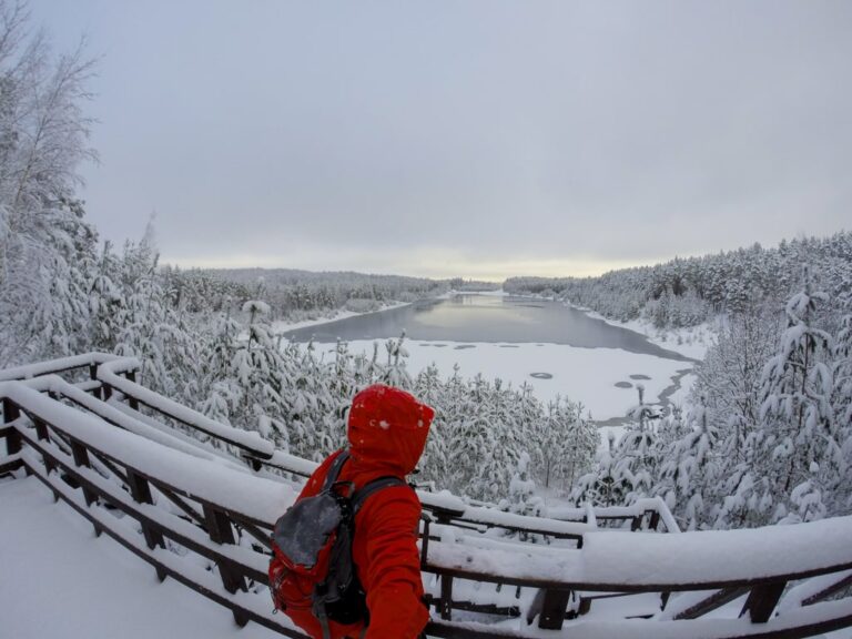 A hiker in a red jacket overlooks the snow covered quarry and forest at Zilo Kalnu Karjers