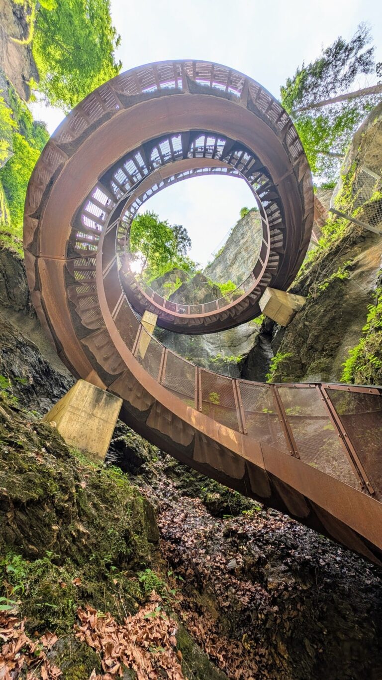 A circular metal staircase climbs between steep, mossy canyon walls at Liechtensteinklamm