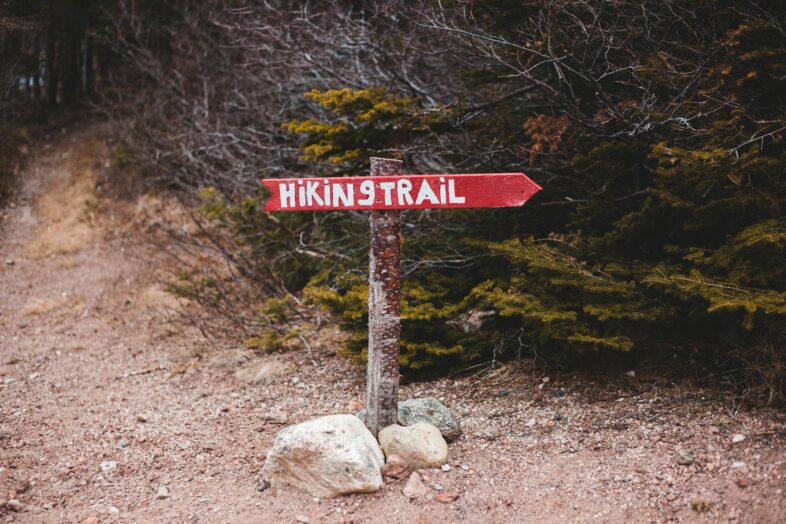 Red hiking trail sign in quiet forest path, inviting adventure and exploration.