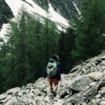 A backpacker hiking through rocky terrain in Champoléon, France with snowy peaks.