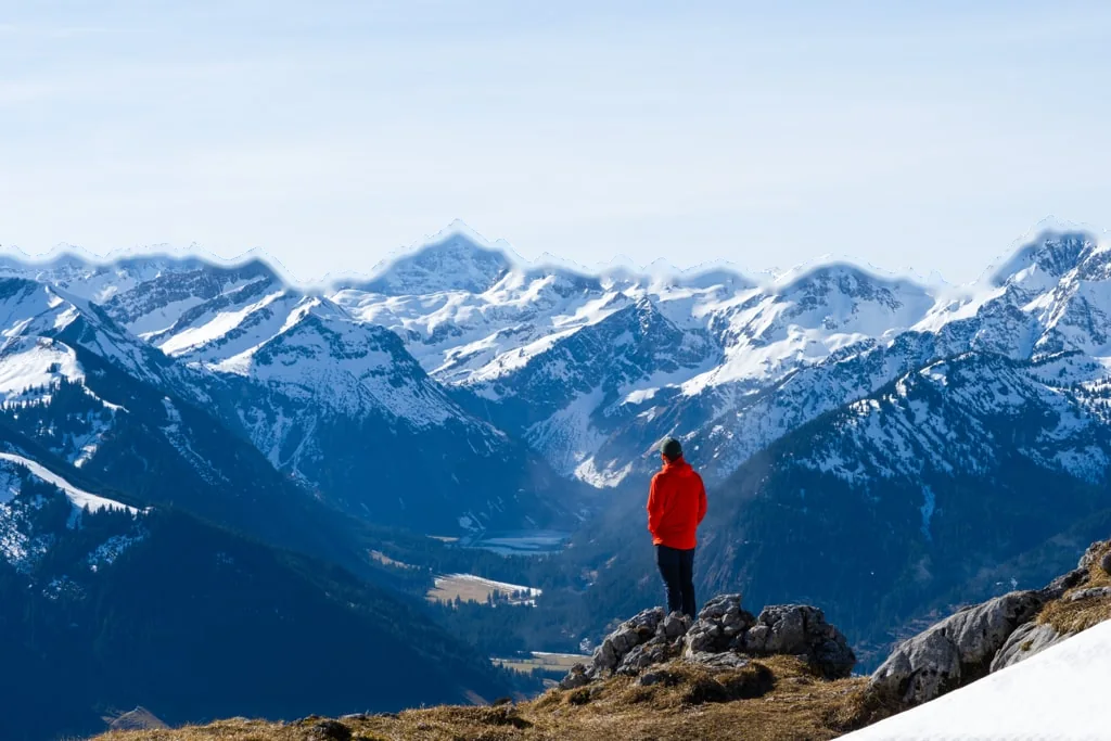 A hiker in red looking out over snowy mountains from Aggenstein