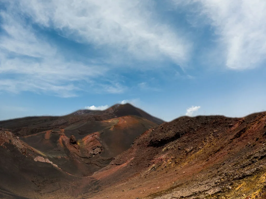 The red and black volcanic slopes of Mount Etna, a hiker small on the rim