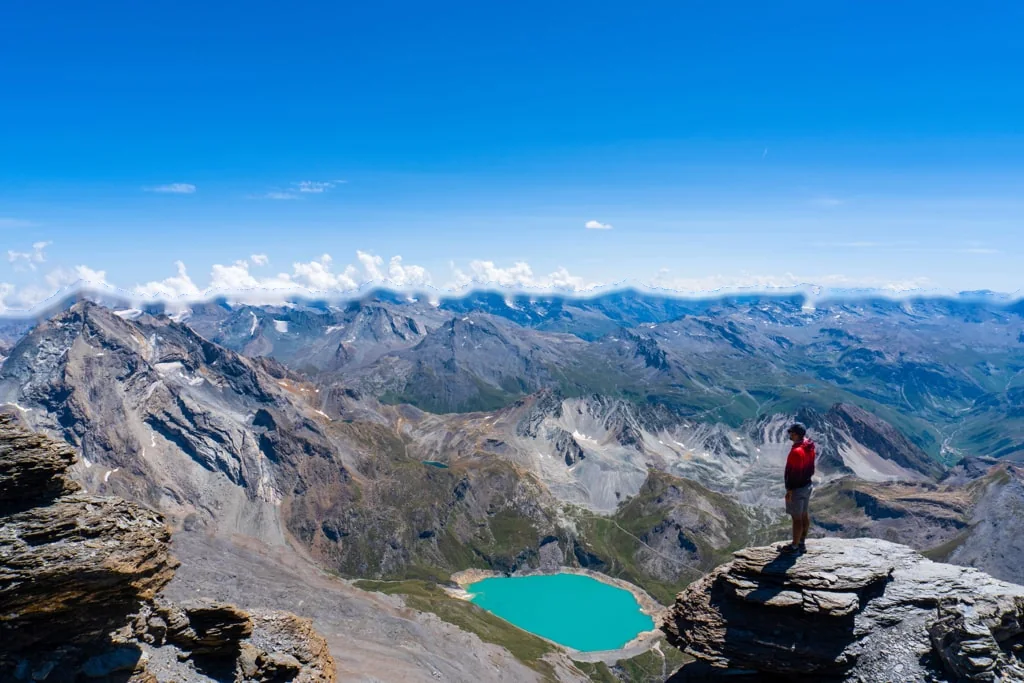 A hiker on a rock above a turquoise lake in the French Alps