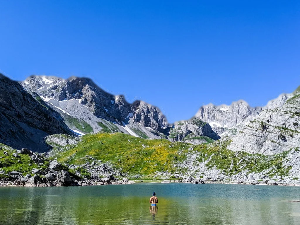 A swimmer standing in a green Jezerca lake below jagged limestone peaks