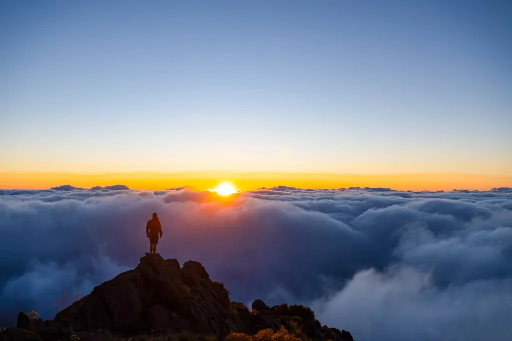 A hiker on a rock above a sea of clouds at sunrise, Madeira