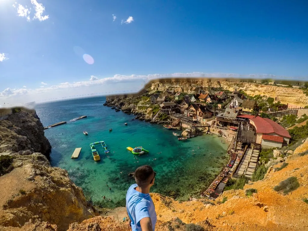 A turquoise cove below the cliffs, with a village of wooden houses, Malta
