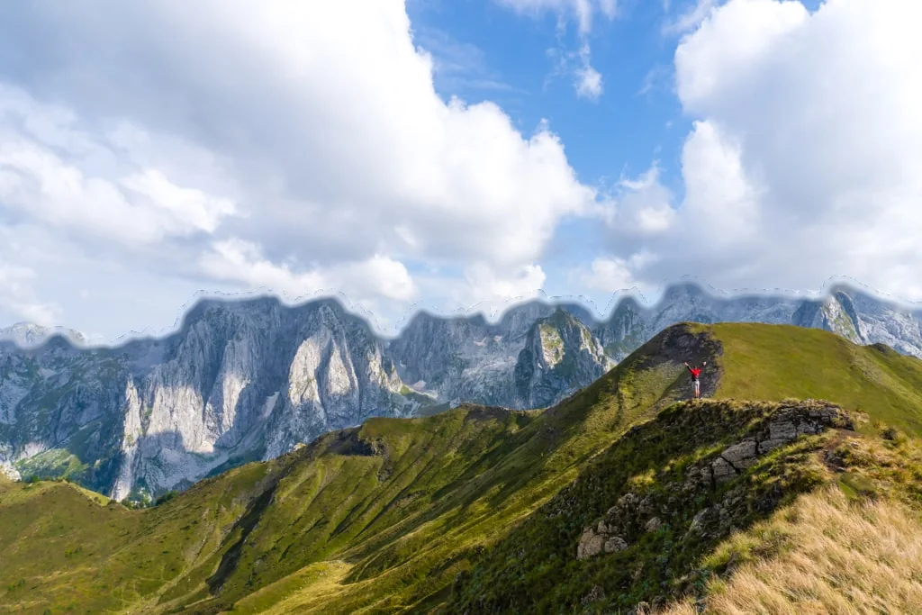 Green slopes below the limestone walls above the Grebaje valley, clouds over the peaks