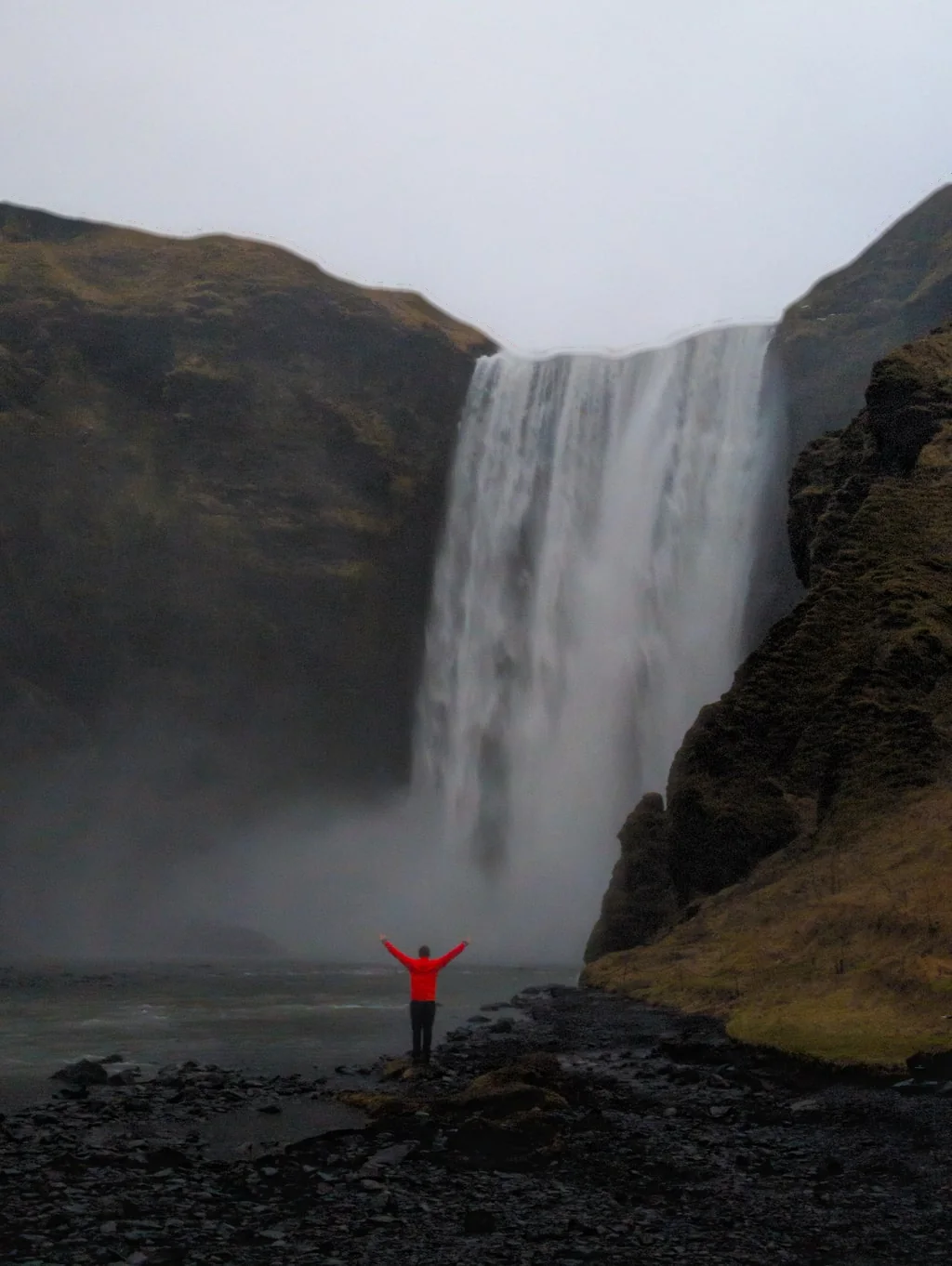 Skógafoss falling from its cliff, a small figure in red below